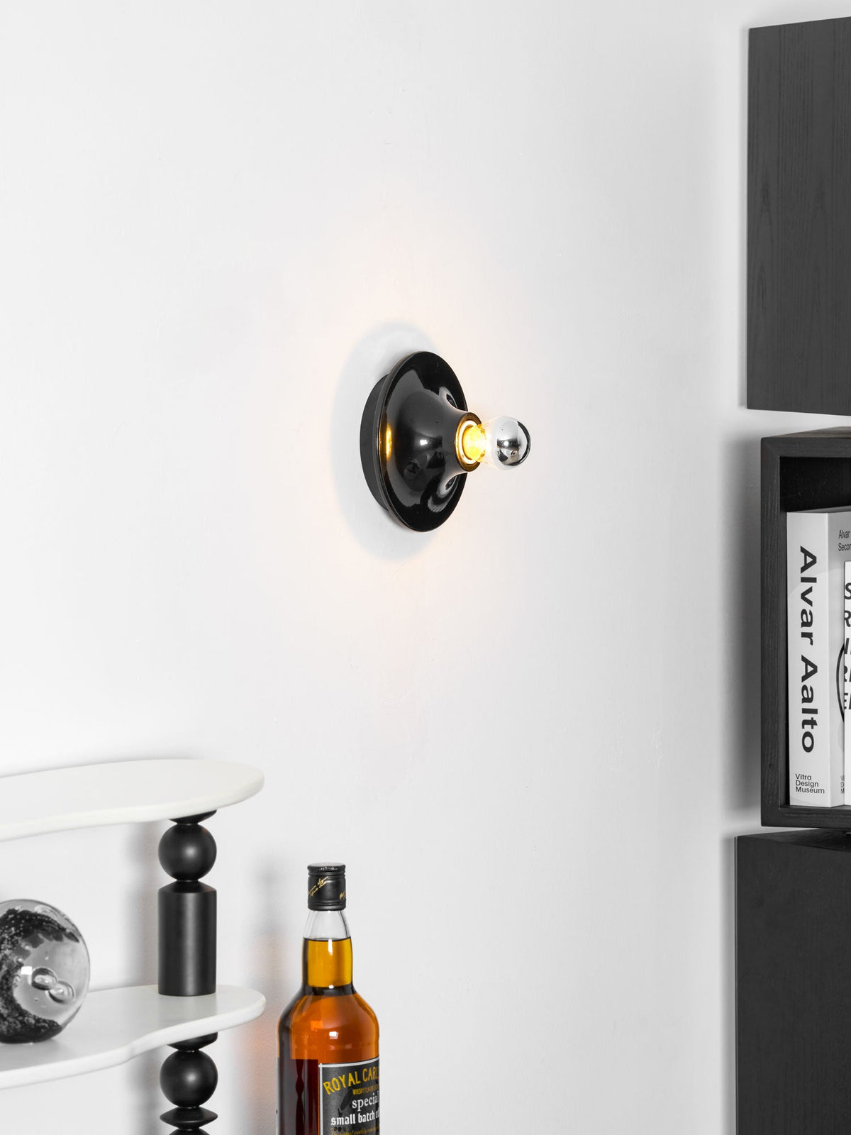 Black disc wall sconce viewed at an angle above bottles on a cabinet