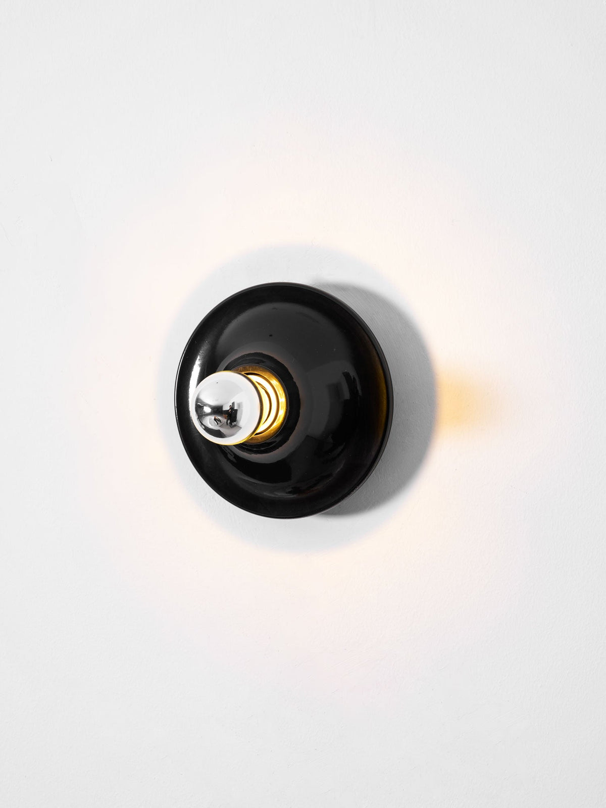 Black disc wall sconce face on lit with warm light on the wall