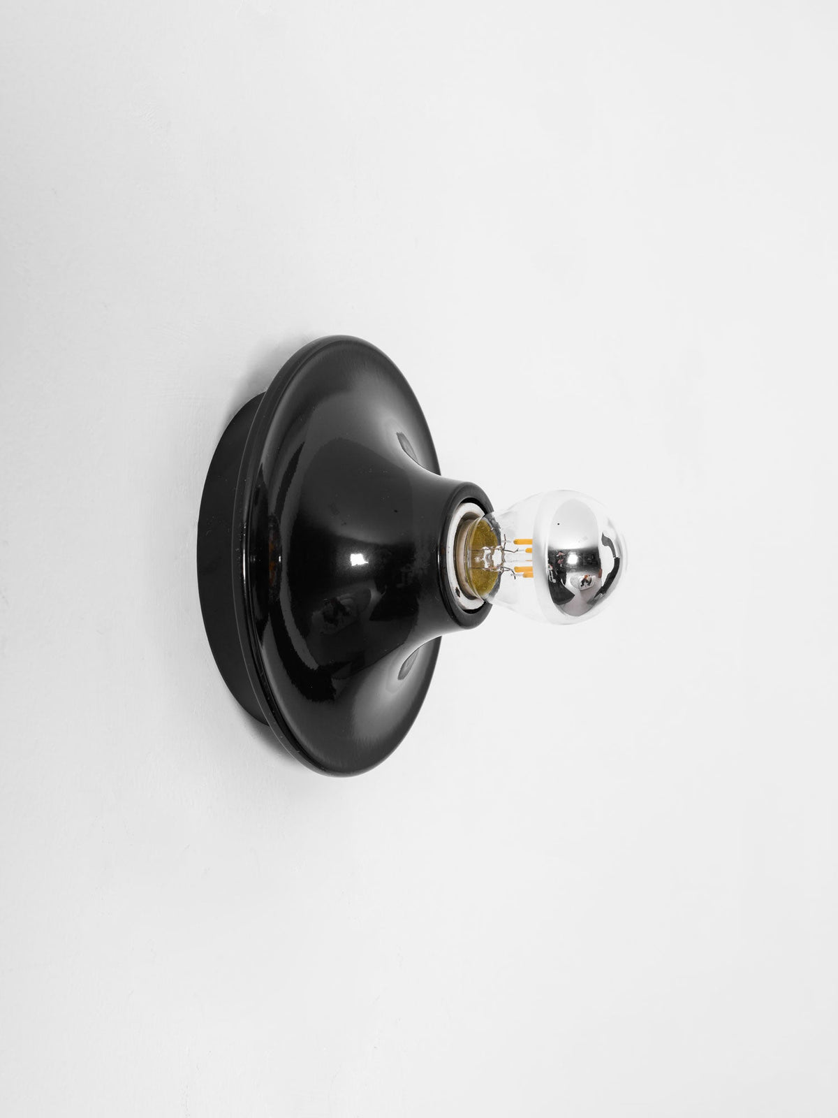 Black disc wall sconce side profile against a plain white wall