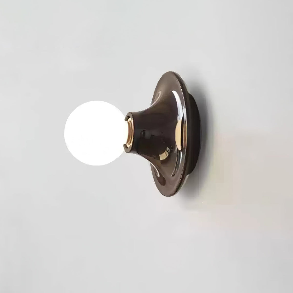 Dark brown disc wall sconce with a lit opal white globe bulb