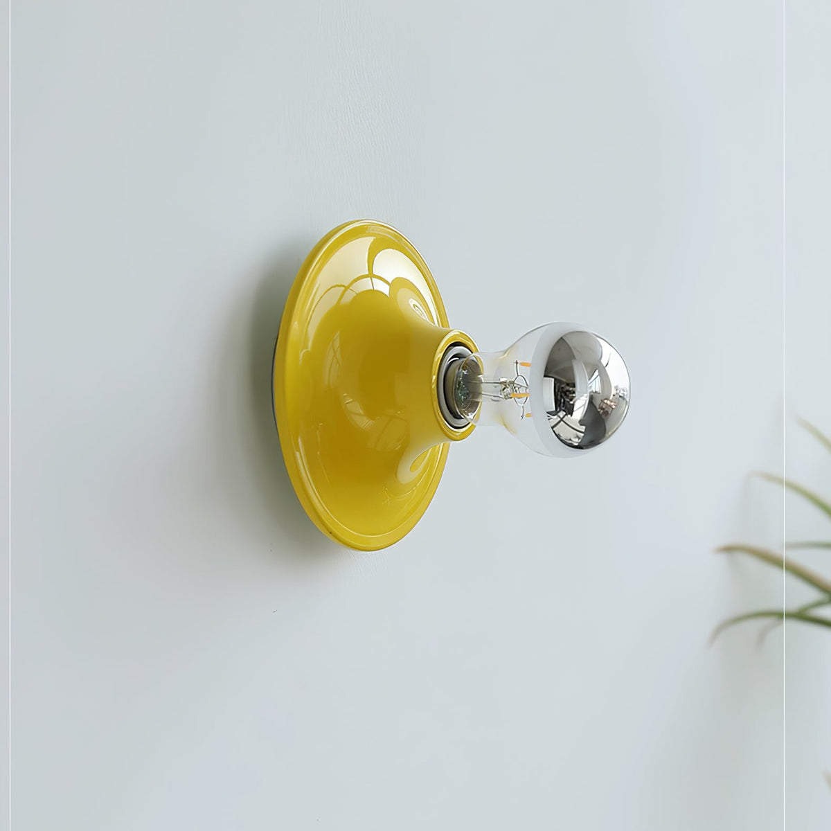 Yellow disc wall sconce with an electroplated bulb on a pale blue wall