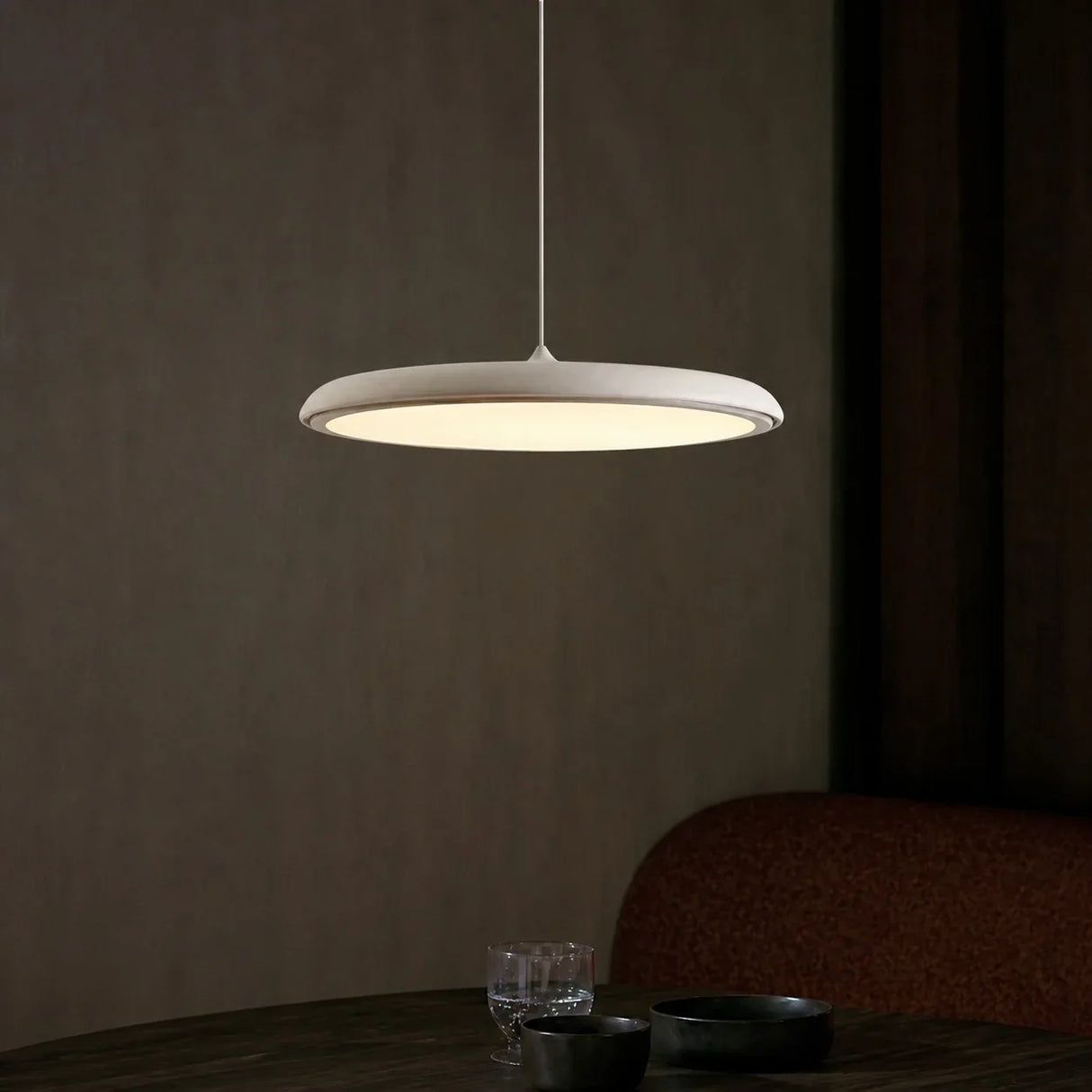 White disc pendant light shown from a raised angle against a plain backdrop