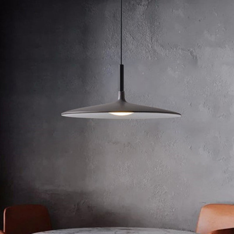 Grey saucer pendant lit against a raw concrete wall and chairs