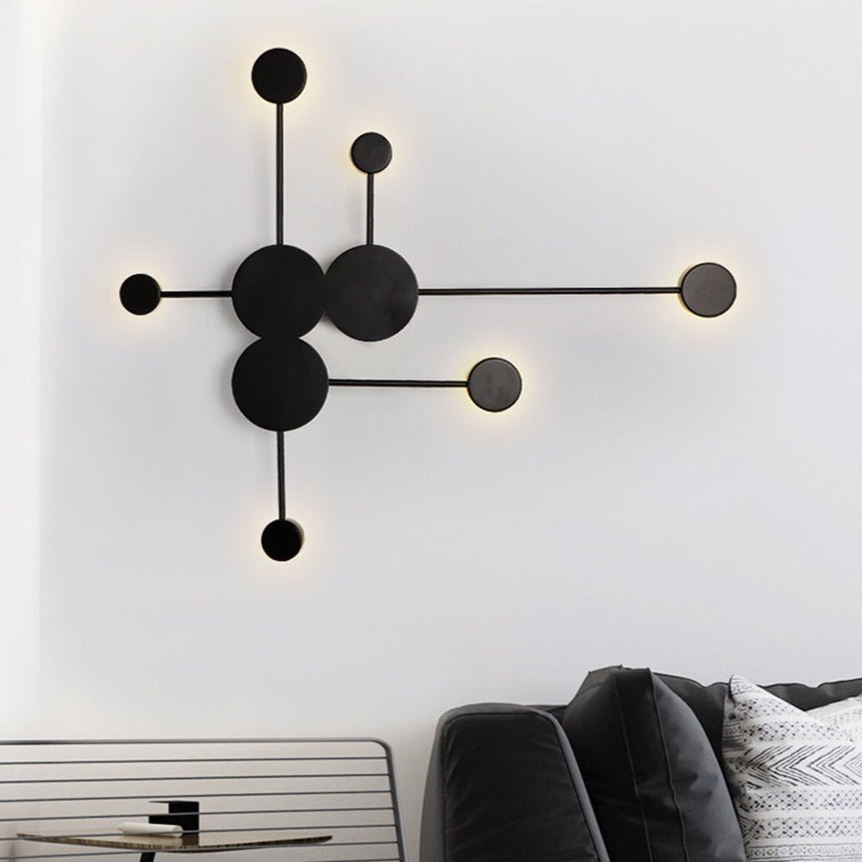 Black six head wall sconce with discs and rods lit on a white wall