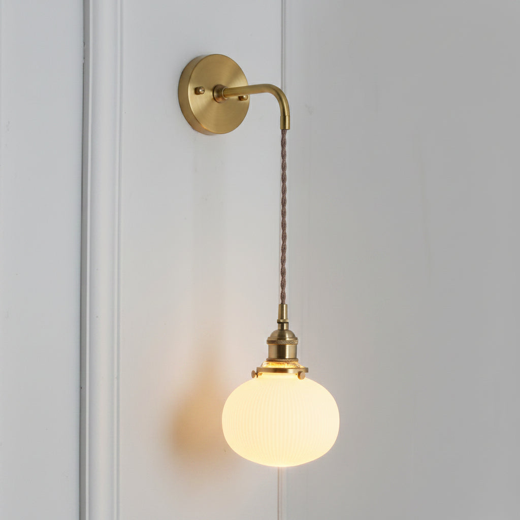 Small round white shade glowing warm on a braided brass cord
