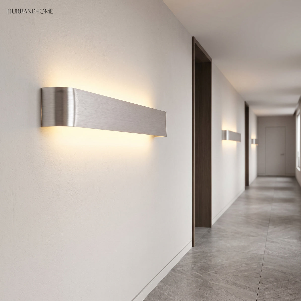 Silver linear wall sconce lit on a white corridor wall