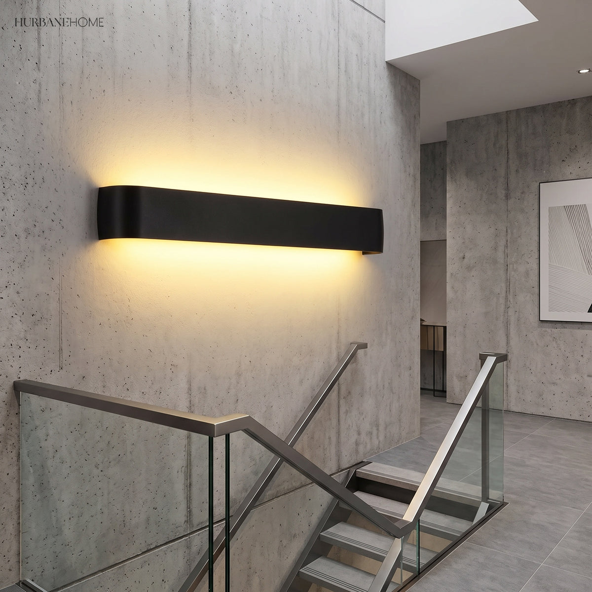 Black linear wall sconce lit on a concrete wall beside a staircase