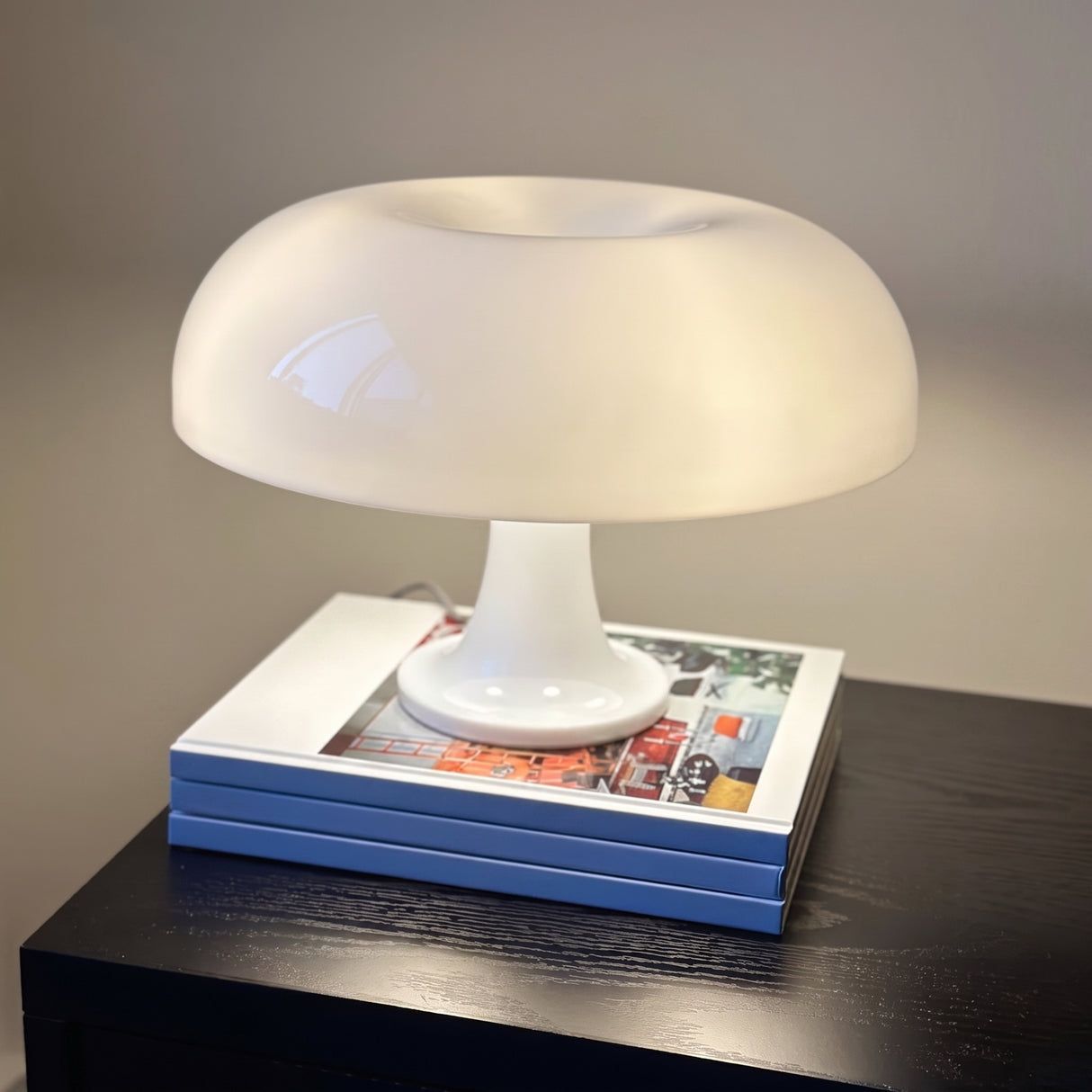 White mushroom table lamp lit on a stack of books on a dark surface