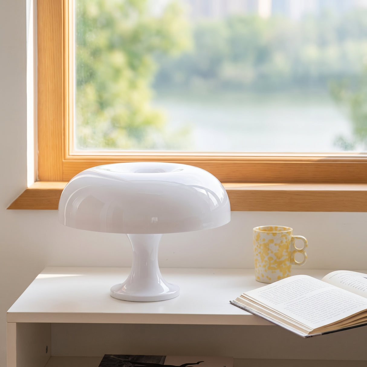 White mushroom table lamp on a desk beside a window with green trees outside