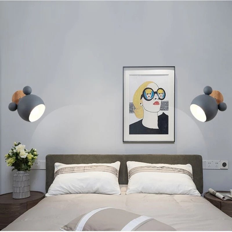 Two grey mouse wall lights lit either side of a bed with framed art