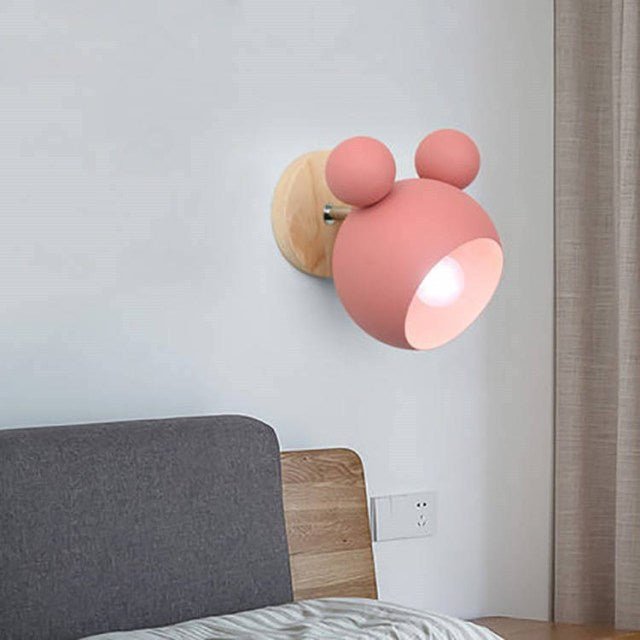 Pink mouse wall light lit above a bed with a grey upholstered headboard