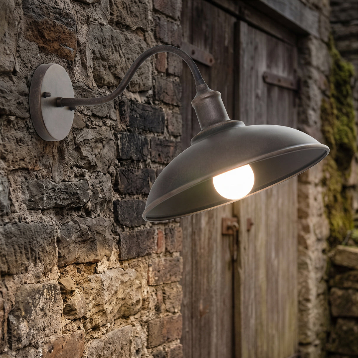 Gooseneck barn light lit on a weathered stone wall beside a door