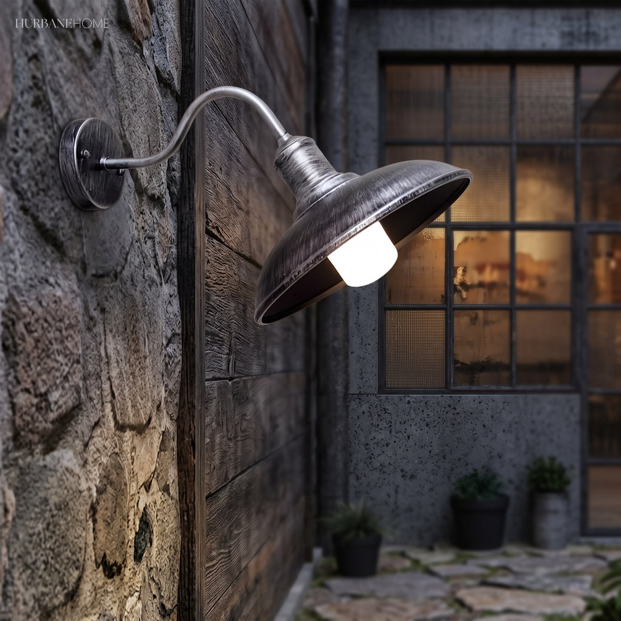 Gooseneck barn light lit on stone beside a black framed window