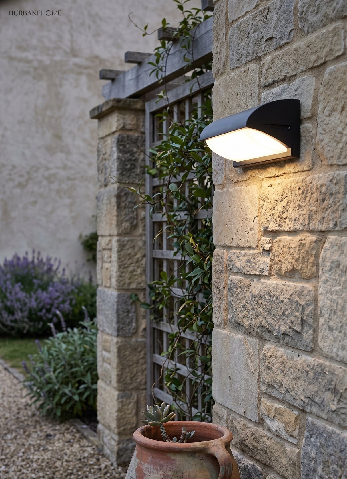 Outdoor light on a stone garden wall beside lavender and a trellis