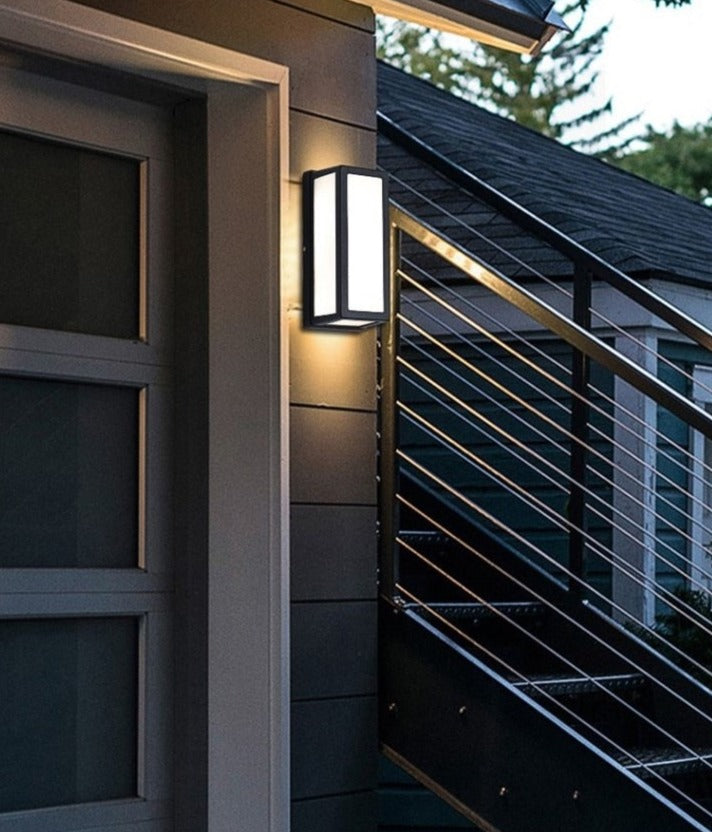 Narrow framed outdoor lantern lit beside a cable stair balustrade