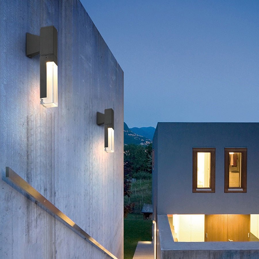 Prism tube wall sconce lit at dusk on a dark clad building wall