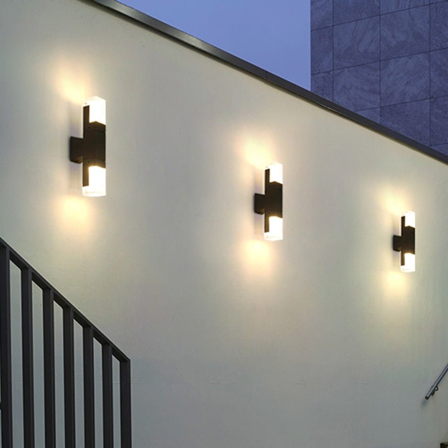 Three prism tube wall sconces lit along a white exterior wall