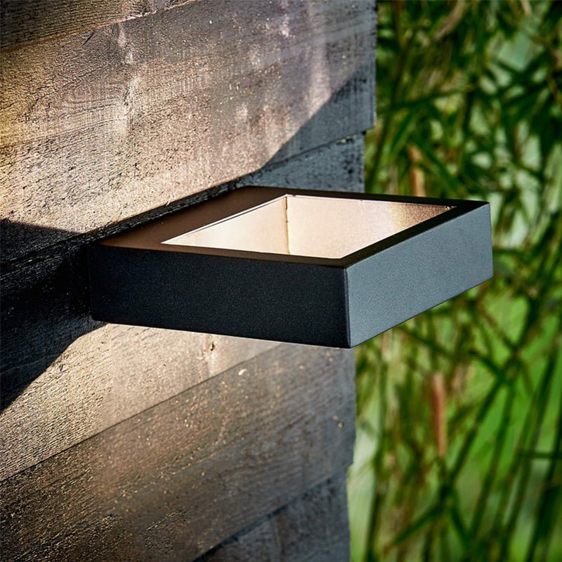 Dark outdoor wall sconce lit on a stone wall beside green bamboo