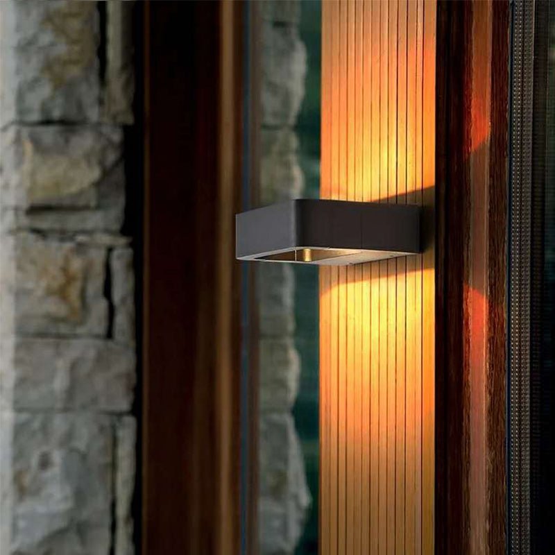 Outdoor wall sconce lit on a ribbed metal wall beside a stone pillar