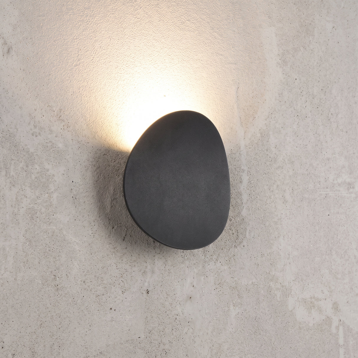Pebble shaped outdoor LED wall light in matt black on a concrete wall