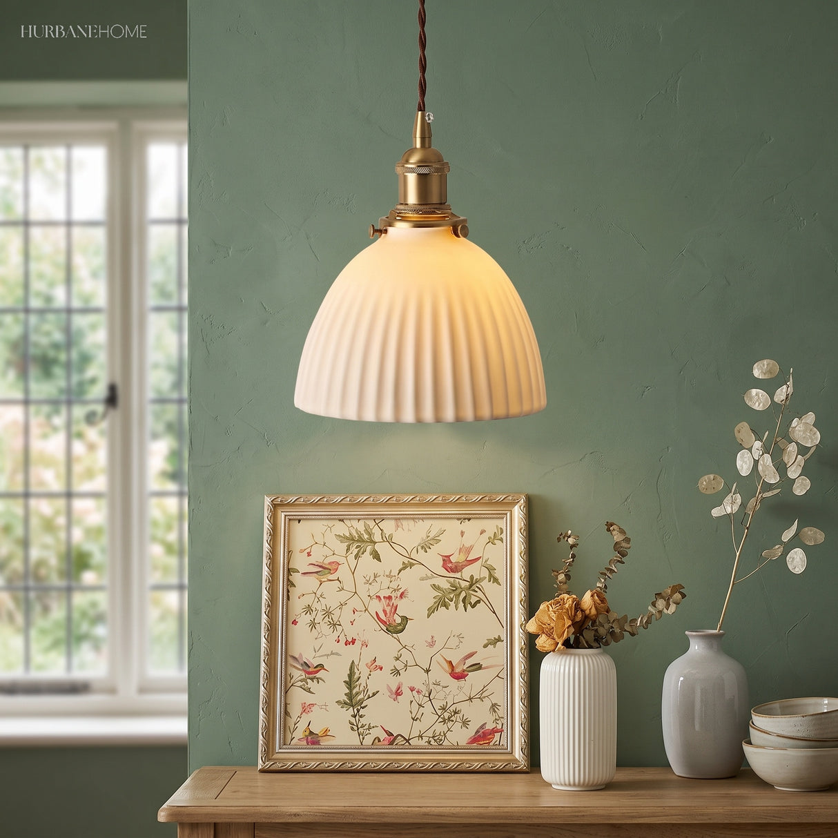Pleated ceramic pendant against a sage wall above framed botanical art
