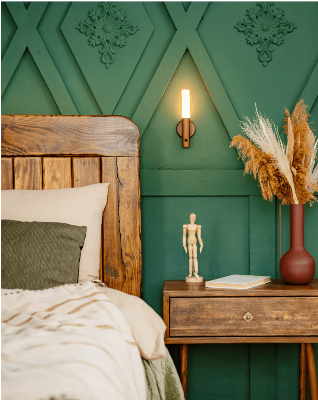 Sconce lit above a wooden bedside table against dark green panelling