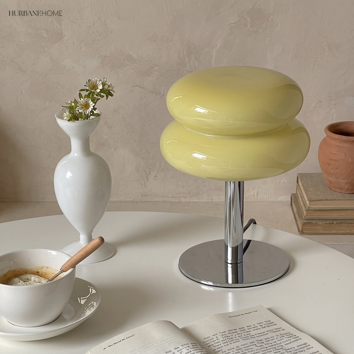 Yellow glass table lamp on a round table with a vase and coffee cup