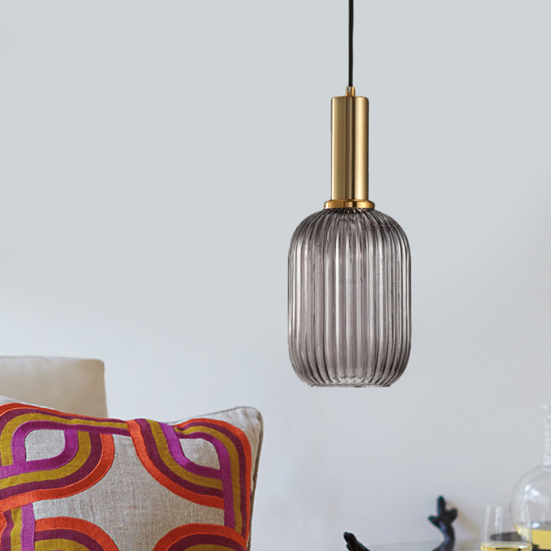 Smoke ribbed pendant lit in a pale room above a bright cushion