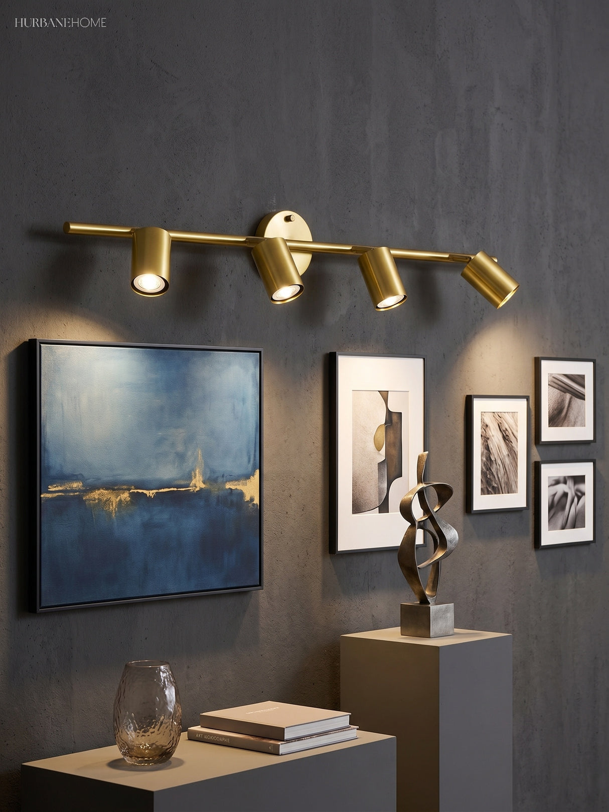 Brass spotlight bar lit on a dark wall above framed pictures and a sculpture
