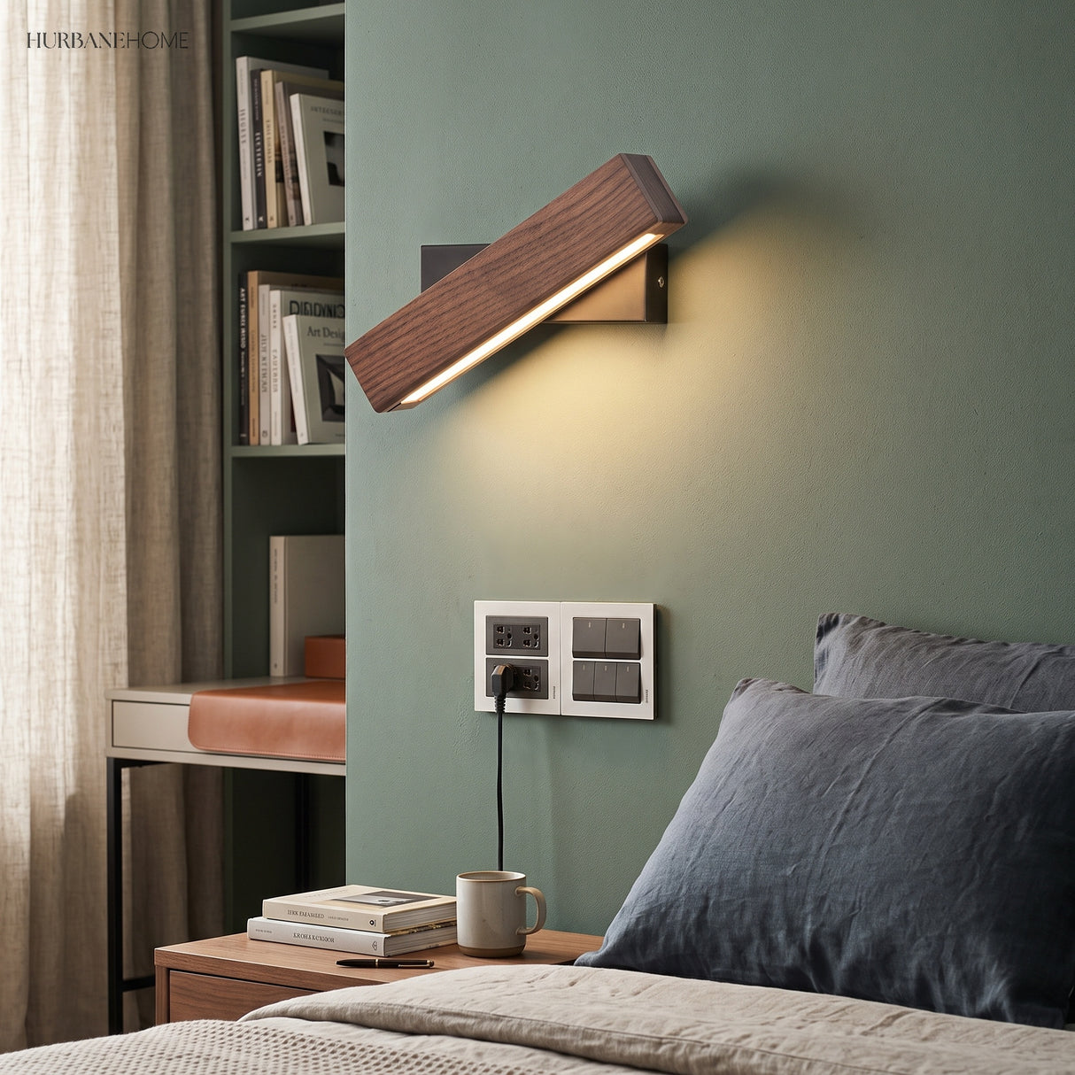 Tilted wood sconce lit on a green wall beside a bed and desk