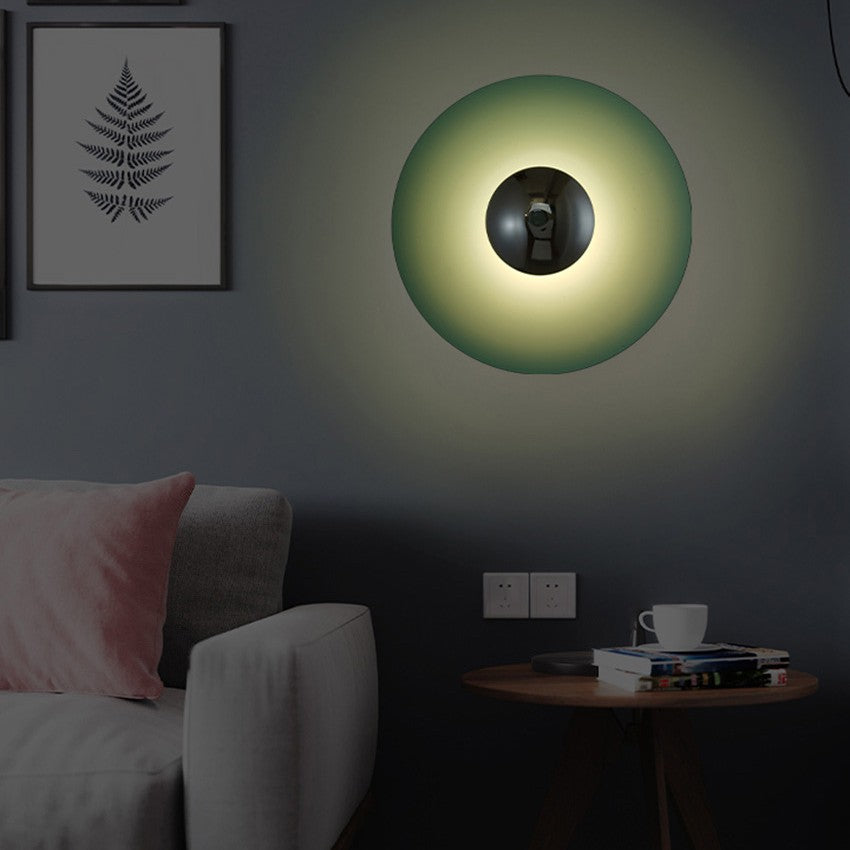Green disc sconce lit on a grey wall beside a framed fern print