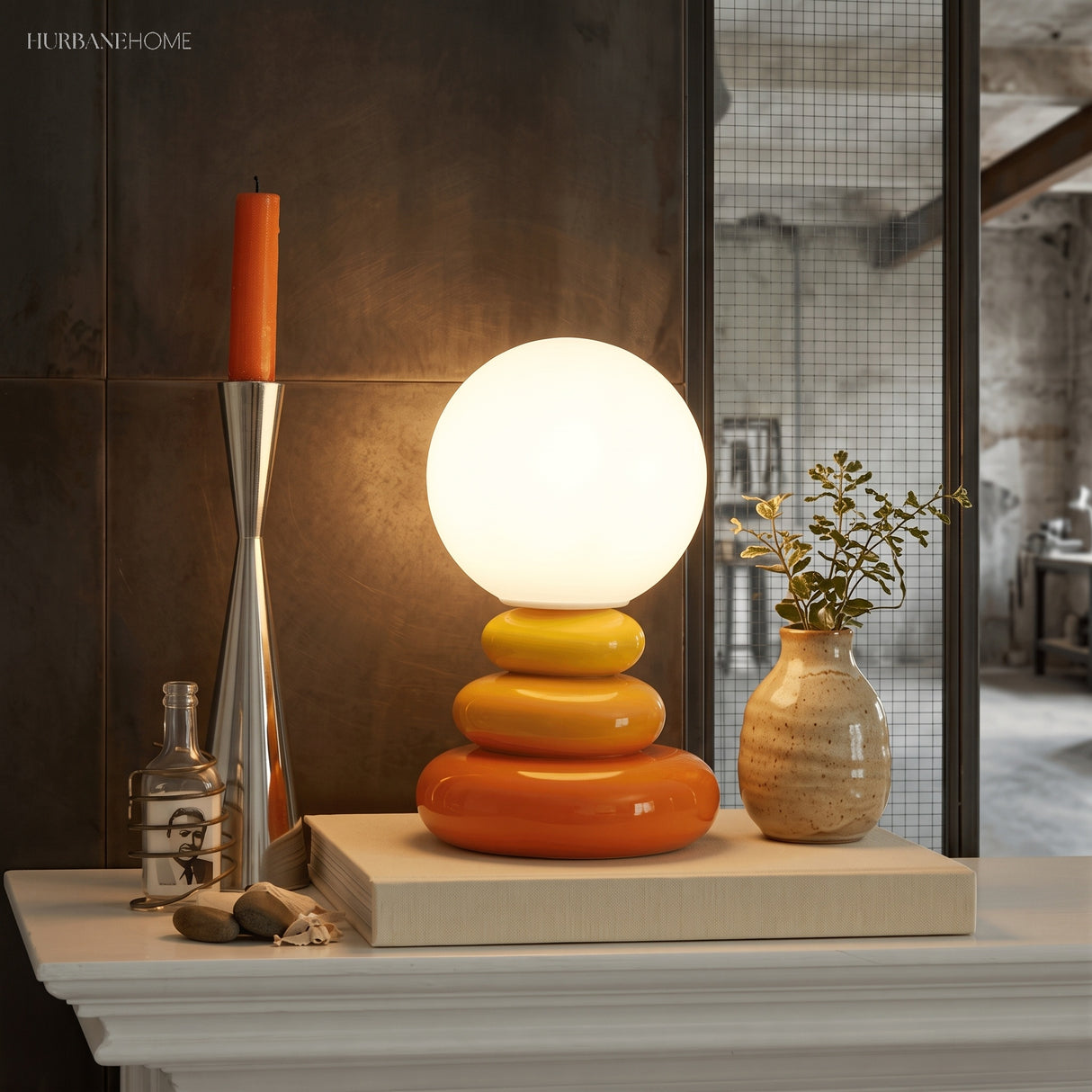 Orange pebble lamp lit beside a candlestick and vase on a pale mantelpiece