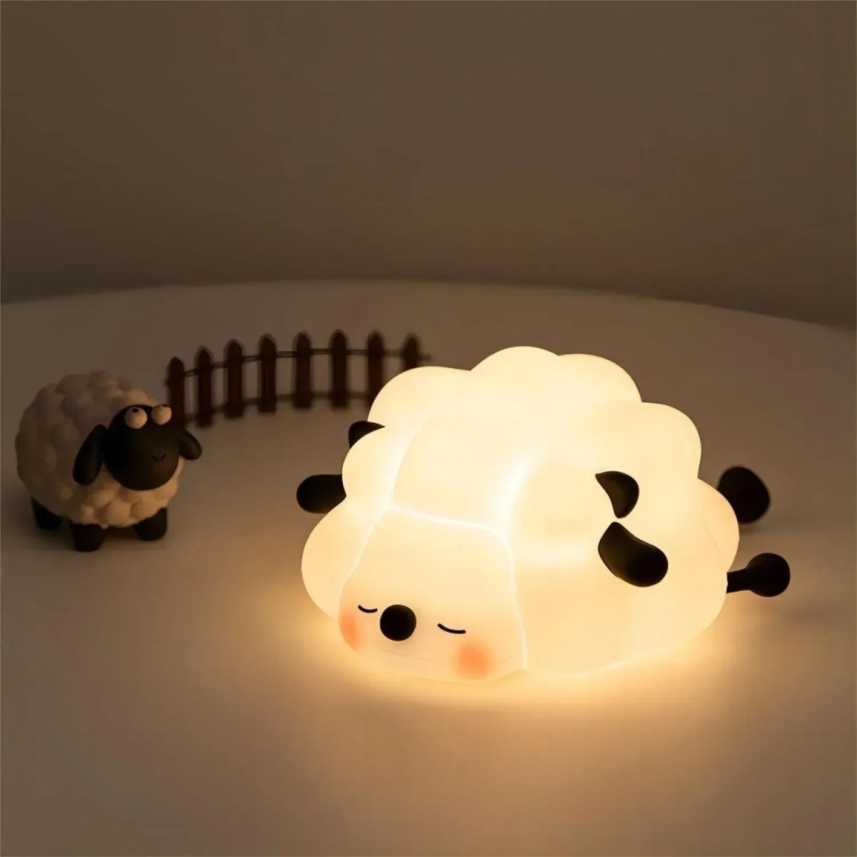 Sheep shaped silicone night light glowing softly beside a small toy sheep