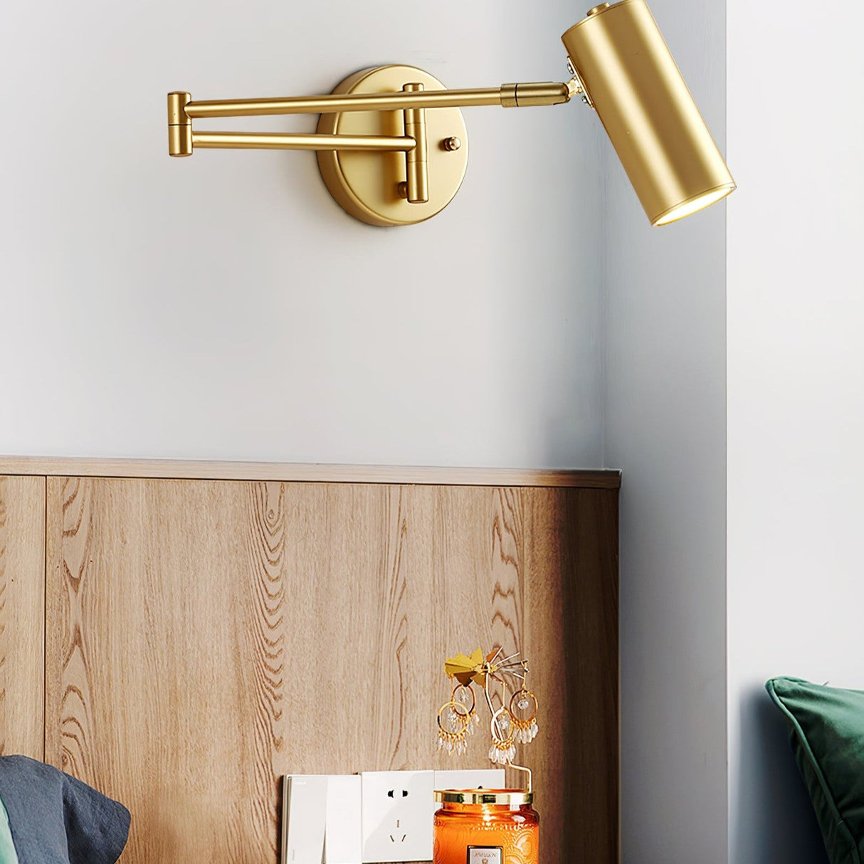 Gold swing arm sconce lit beside a wooden headboard