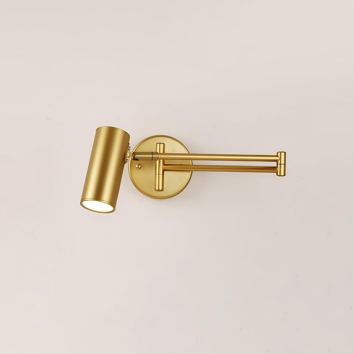 Gold swing arm sconce extended on a plain cream wall