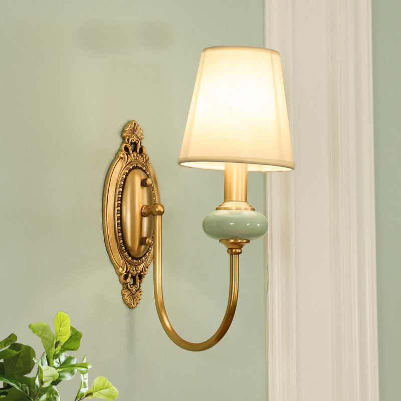 Single gold sconce lit warm on a pale green painted wall