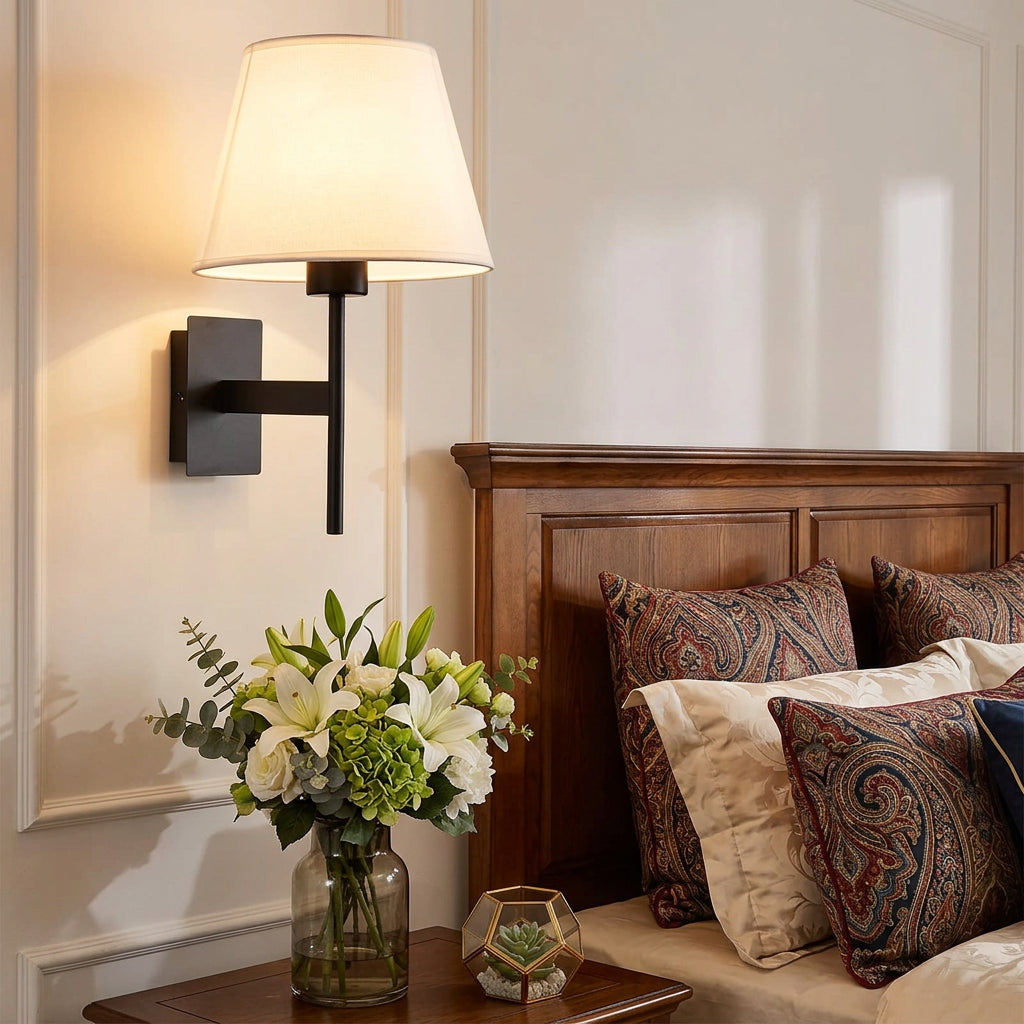 Wall sconce above a wooden headboard with flowers on the bedside table