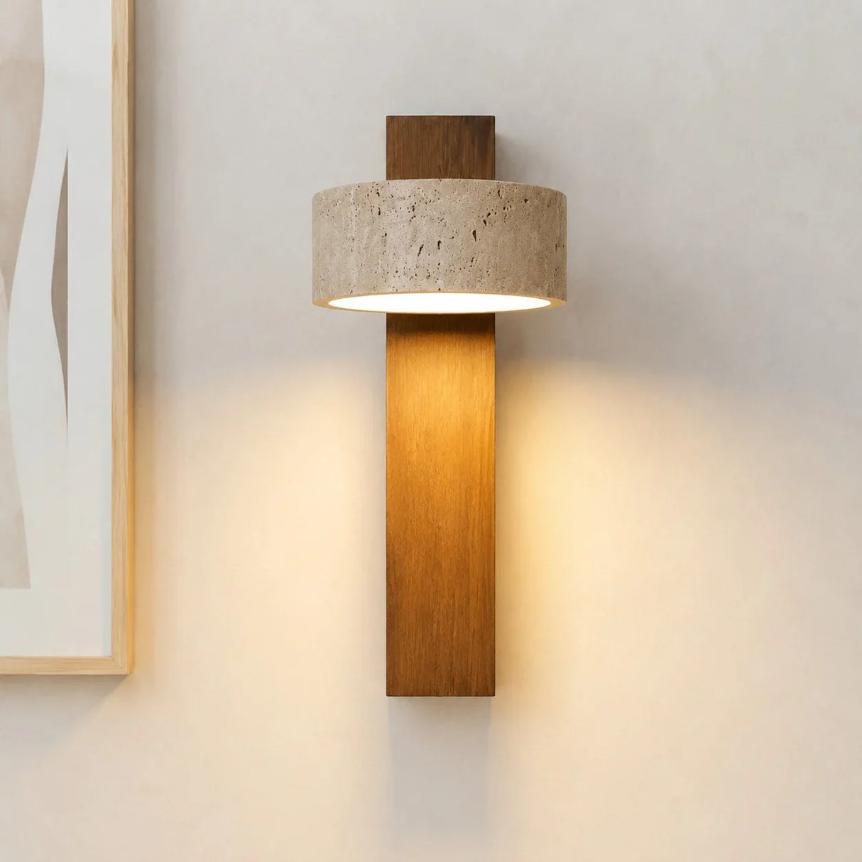 Wood wall sconce with upright travertine drum shade beside a framed print