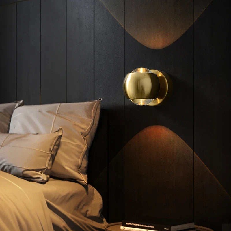 Gold orb sconce lit above a bed with linen pillows and dark panelling