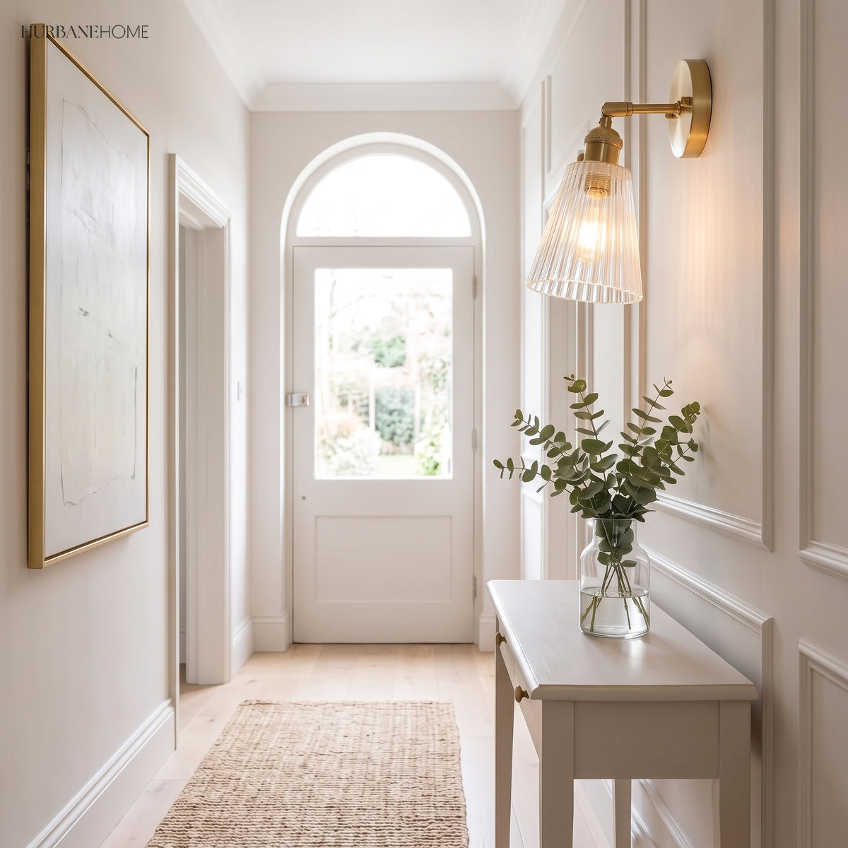 Brass wall sconce lighting a bright hallway beside an arched front door
