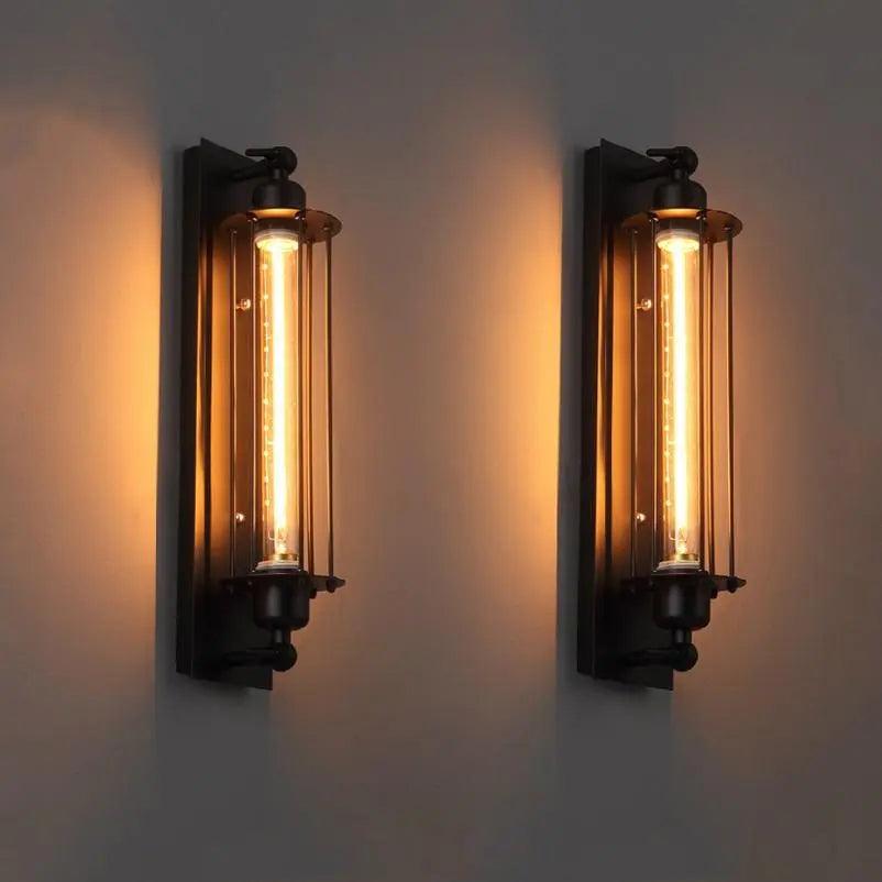 Two black cage sconces lit warm side by side on a grey wall