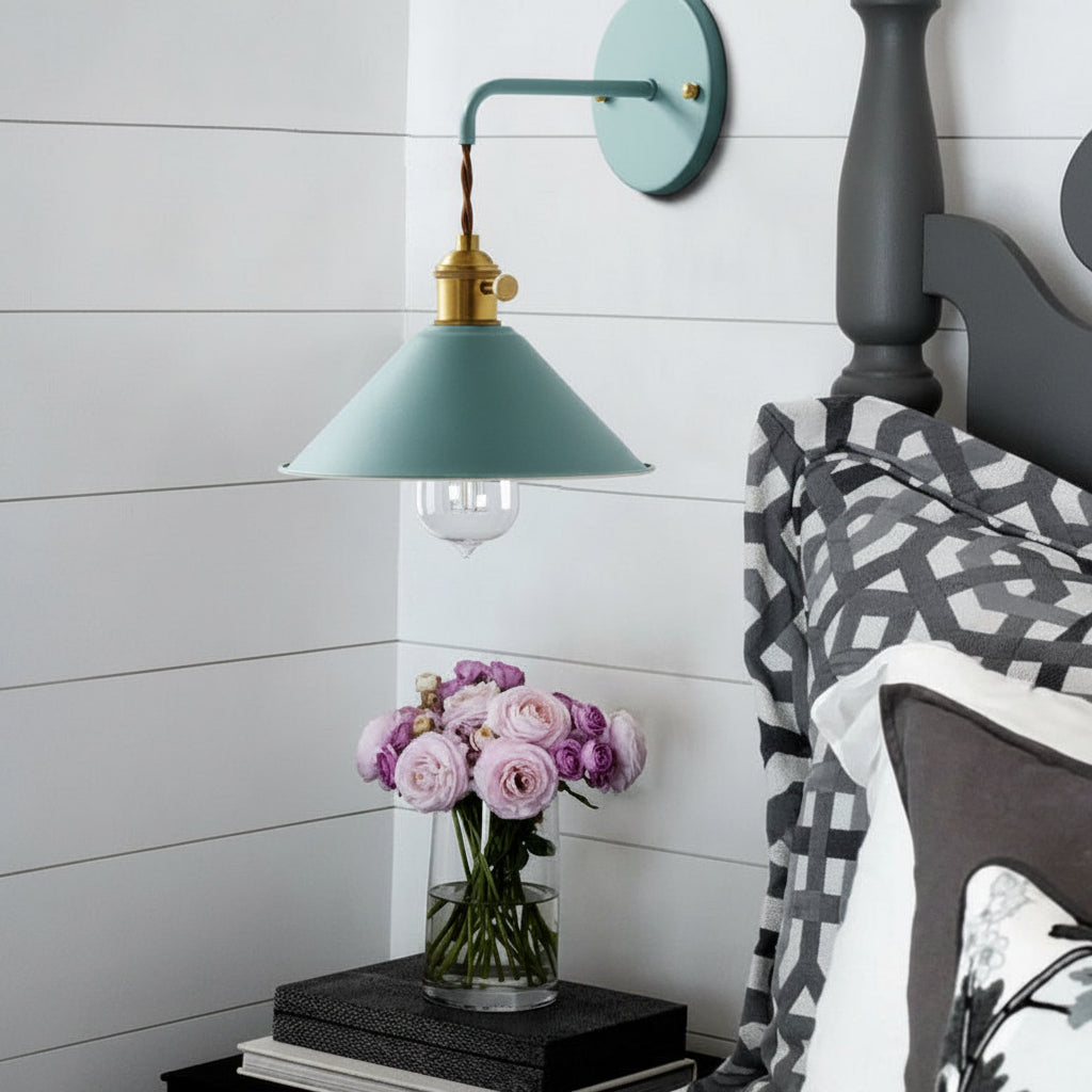 Blue cone shade sconce lit above a bed with patterned bedding