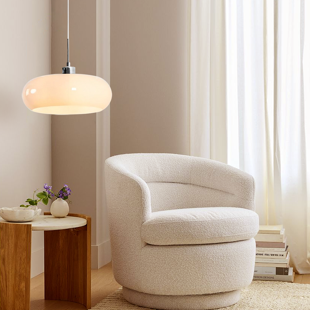 White glass pendant light glowing over a side table beside a boucle armchair
