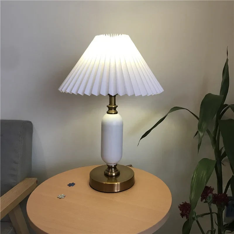 White pleated table lamp lit on a brass column base