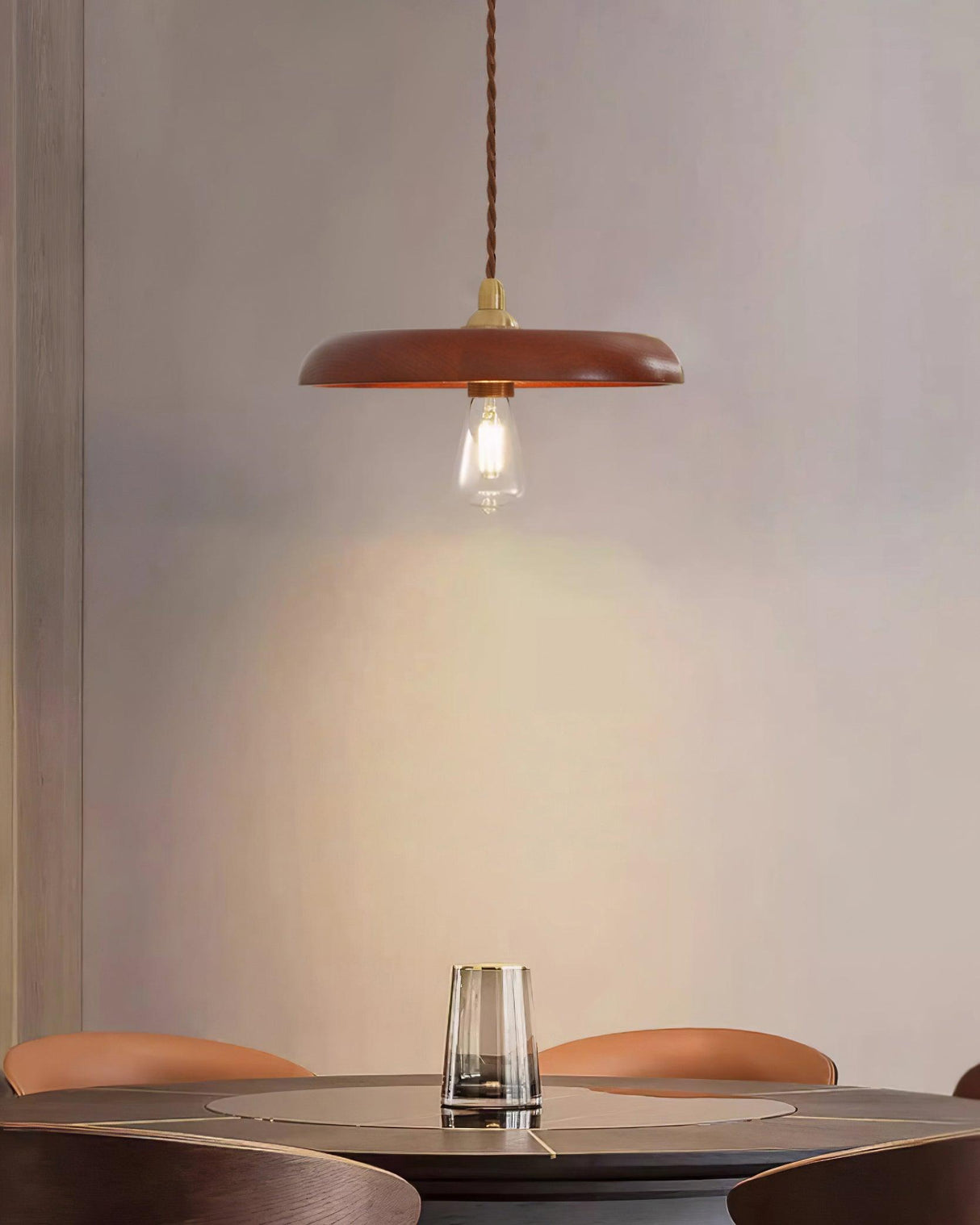 Wood disc pendant lit above a round cafe table with a glass tumbler