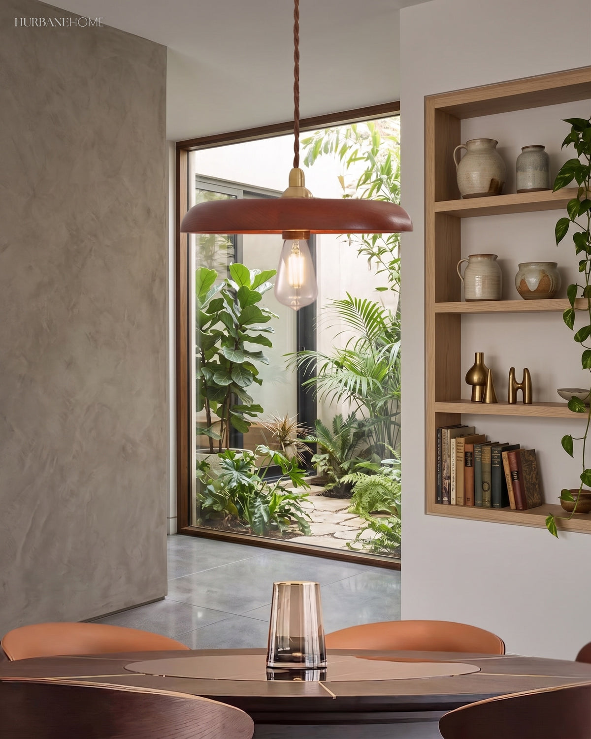 Wood pendant light hanging over a small round table beside a planted courtyard