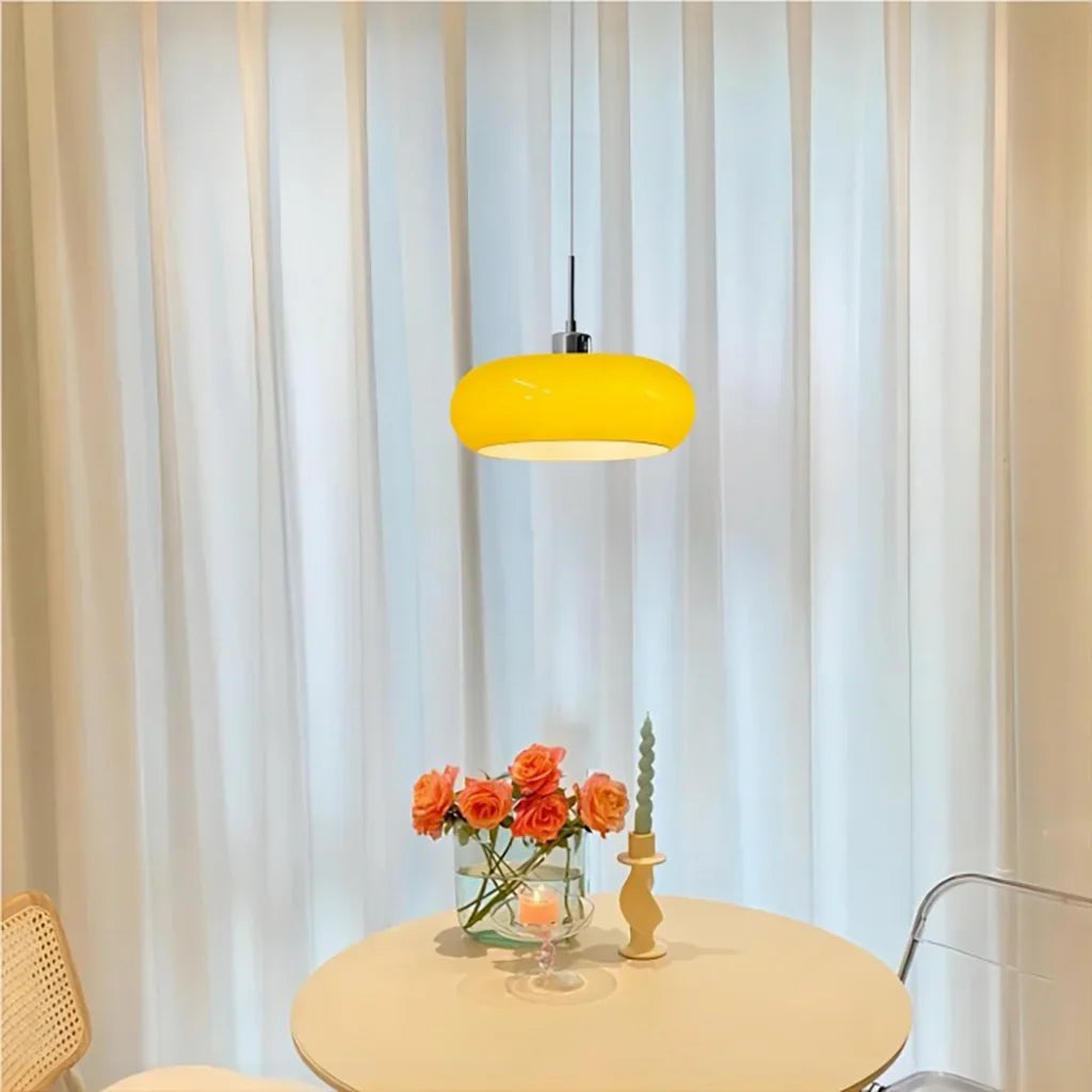 Yellow lit glass pendant light over a round table with sheer curtains