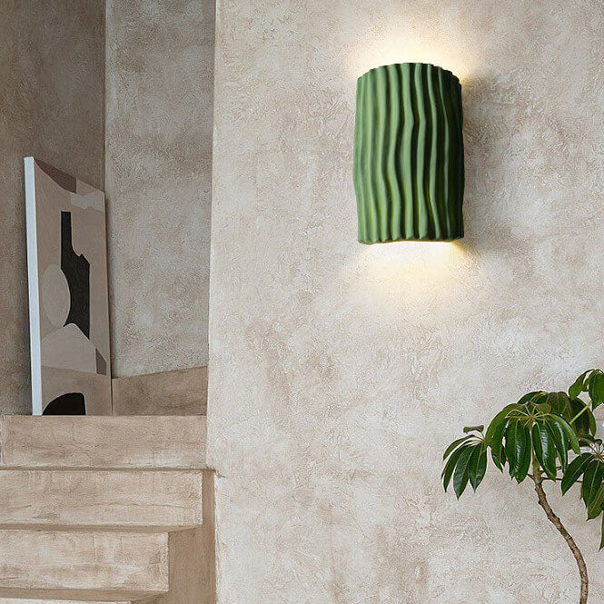 Cream textured half cylinder wall sconce glowing up and down on plaster