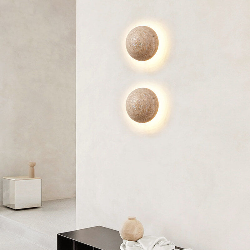 Two travertine LED wall sconces lit on a bright white wall in a hallway
