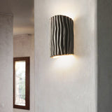Gray textured wall sconce on a plaster corner wall near a window